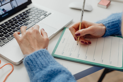 Woman writing plans in a printed weekly planner template with computer aside